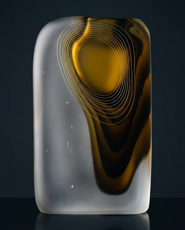 A sleek, abstract glass sculpture featuring swirling patterns of amber and transparent hues, set against a dark background. The mood is contemporary and sophisticated, with smooth lines creating a sense of fluidity and elegance.