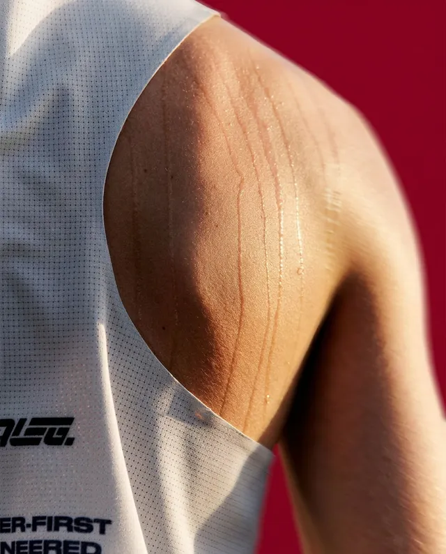 A close-up editorial photograph captures the glistening skin of an athletic shoulder, revealing droplets of sweat and highlighting the contours of the muscle. The vibrant red background enhances the intensity of the moment, conveying a mood of determination and effort.
