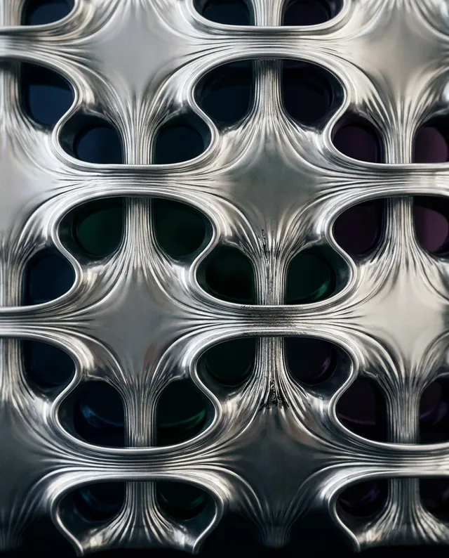 This close-up image showcases a sleek, metallic surface with intricate, organic patterns interwoven throughout, creating a sense of fluidity and modernity. The dominant colors are muted silvers with hints of deep blues and purples, lending a sophisticated and contemporary mood to the composition.