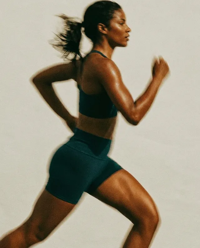 A dynamic editorial photograph captures a muscular woman sprinting, showcasing athleticism and determination. The image has a warm, muted color palette with soft highlights, conveying an energetic yet focused mood.