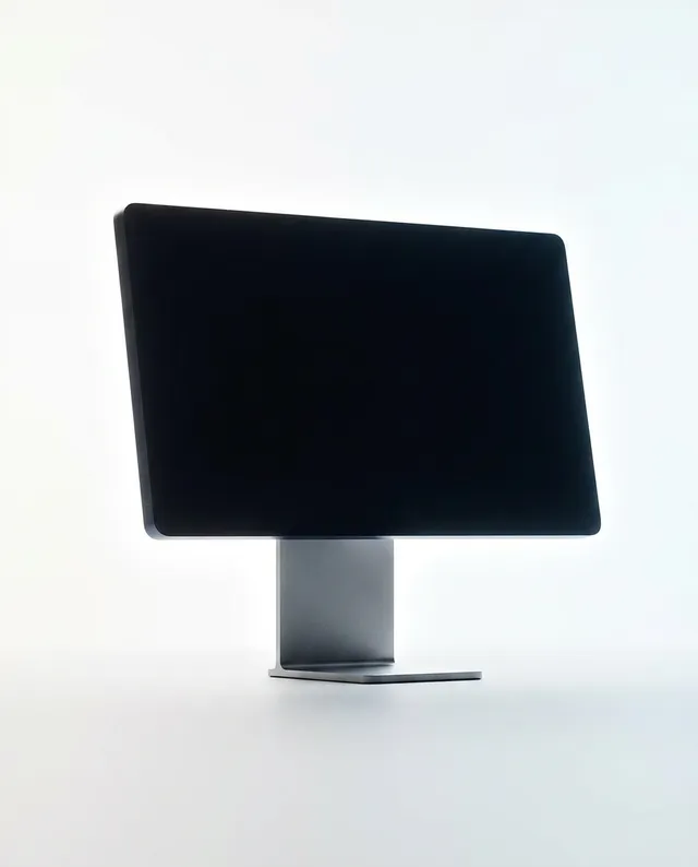 A minimalist editorial photography image features a sleek, modern computer monitor silhouetted against a soft, light background. The dominant colors are shades of black and white, evoking a clean and contemporary mood.
