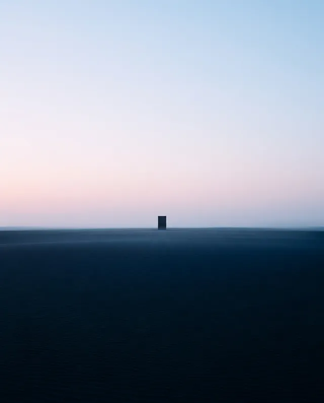 A minimalist landscape photograph featuring a solitary black structure against a soft gradient sky at dawn, evoking a sense of solitude and tranquility. The dominant colors are cool blues and gentle pinks, creating a serene and contemplative mood.