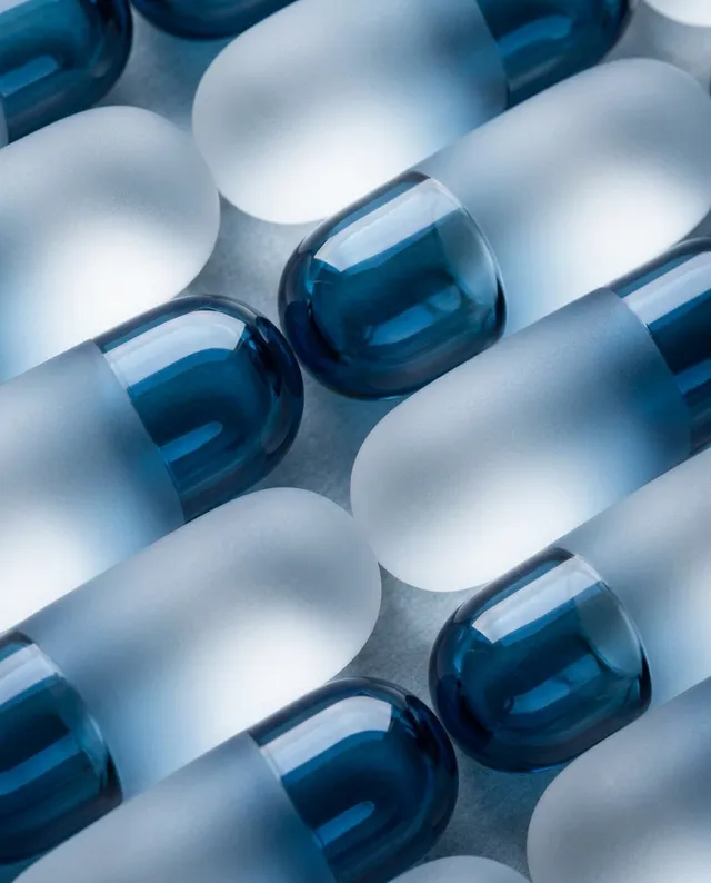 This editorial photography piece features a close-up arrangement of frosted and glossy blue capsules, creating a serene and modern aesthetic. The dominant colors are various shades of blue, evoking a tranquil and clinical mood.
