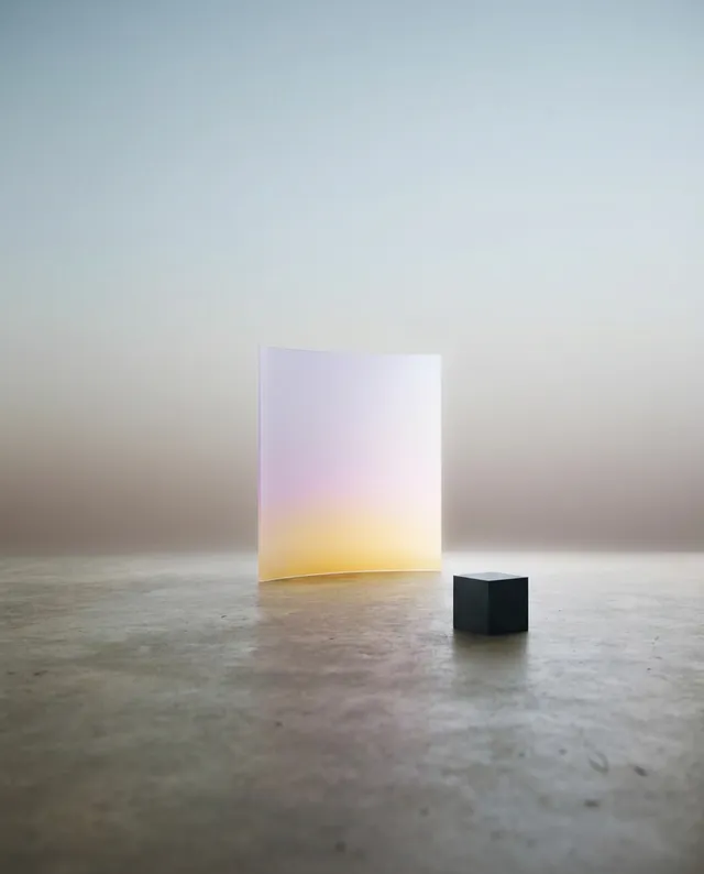 A serene, minimalistic still life featuring a translucent, gradient panel in soft pastel hues of lilac and yellow, paired with a stark black cube. The overall mood is calm and ethereal, set against a softly blurred background with subtle earthy tones.