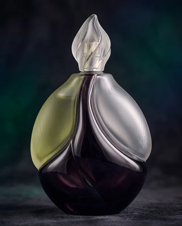 This editorial photograph showcases an elegantly designed glass perfume bottle with a swirling, organic form. The dominant colors are deep purple and soft green, exuding a sophisticated and luxurious mood.