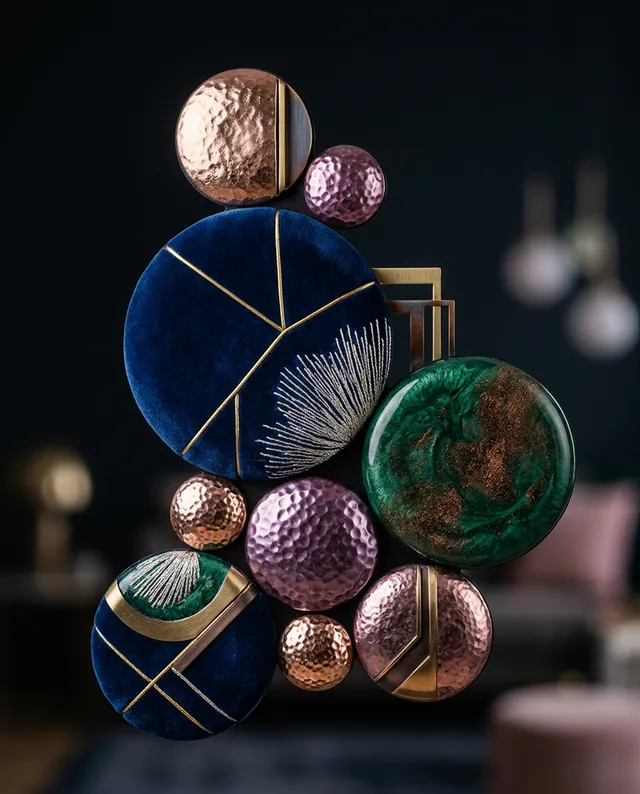 A striking still life composition features a series of textured circular forms in deep blue, green, and metallic hues, layered with intricate patterns and reflective surfaces. The elegant arrangement creates a luxurious and contemporary mood, set against a dark backdrop that enhances its vibrancy.