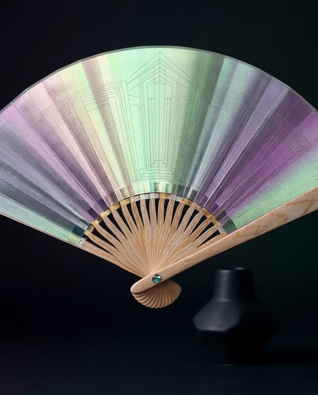 This elegant still life features a stunning iridescent fan, radiating soft pastel hues against a dark background, complemented by a minimalist black vase. The composition conveys a sense of sophistication and tranquility, blending traditional craftsmanship with contemporary design elements.