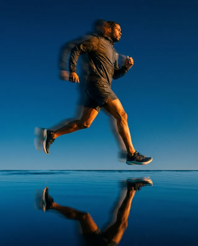 A dynamic editorial photograph captures a runner in motion against a vibrant blue sky, with reflections in a still surface enhancing the sense of speed and energy. The image conveys determination and freedom, dominated by cool tones of blue and hints of warmth from the runner’s attire.