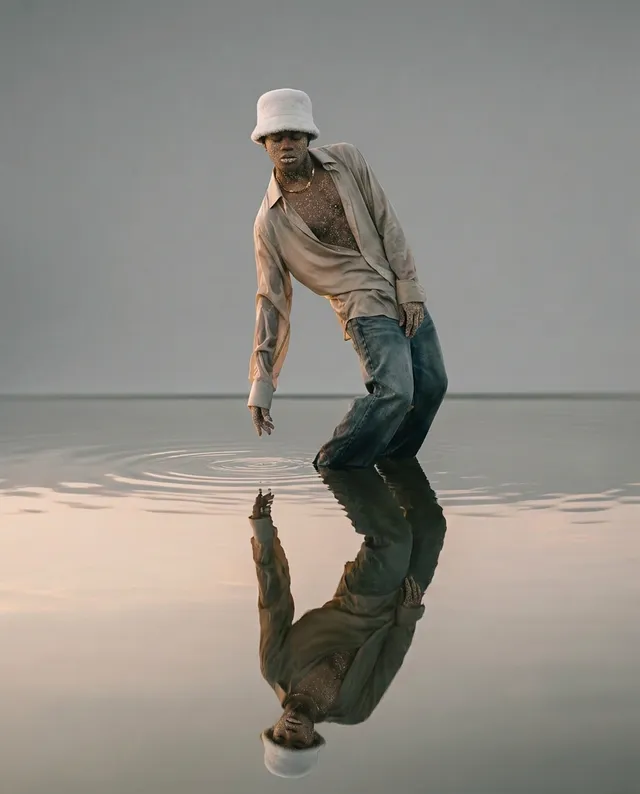 A full-figure portrait of a man interacting with water, creating ripples, captured in a serene and reflective moment. The image features muted earth tones and a soft, dreamy aesthetic.