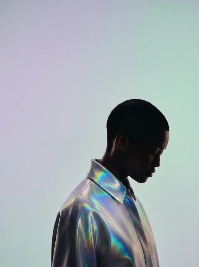 A side profile of a person wearing a holographic shirt, captured in a minimalist editorial style. The mood is serene, with soft pastel colours creating an ethereal ambiance.