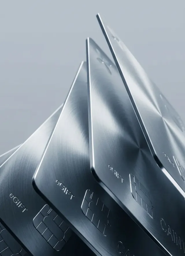 A sleek, editorial-style photograph captures metallic gift cards stacked at an angle, emphasizing their smooth, reflective surfaces. The dominant colors are shades of silver and gray, conveying a modern and sophisticated mood.