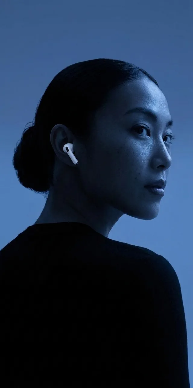 A captivating editorial photograph featuring a woman with a sleek bun, adorned with white AirPods. The image is dominated by cool blue tones, creating a modern and sophisticated atmosphere.