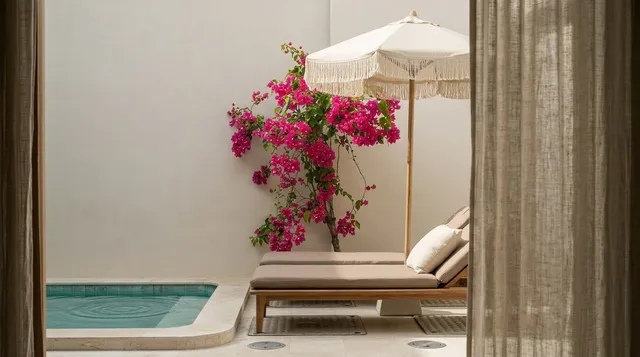 A serene editorial photograph captures a peaceful outdoor space featuring a sunbed beside a tranquil pool, framed by delicate curtains. The mood exudes relaxation, complemented by the vibrant pink bougainvillea and soft neutral tones of the surrounding decor.