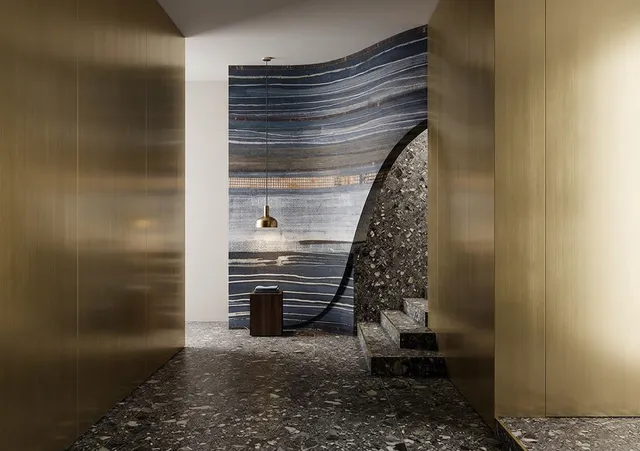 A sleek, modern hallway showcases a striking blend of textured blue and earthy stone walls, illuminated by a warm pendant light. The mood is sophisticated and minimalist, highlighted by dominant gold and dark hues.