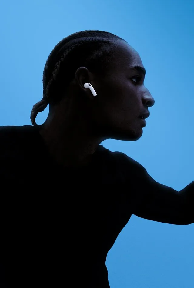 A profile portrait of a person wearing wireless earbuds against a vibrant blue background, captured in a sleek, editorial photography style. The image conveys a modern and stylish mood, highlighted by contrasting light and shadow.
