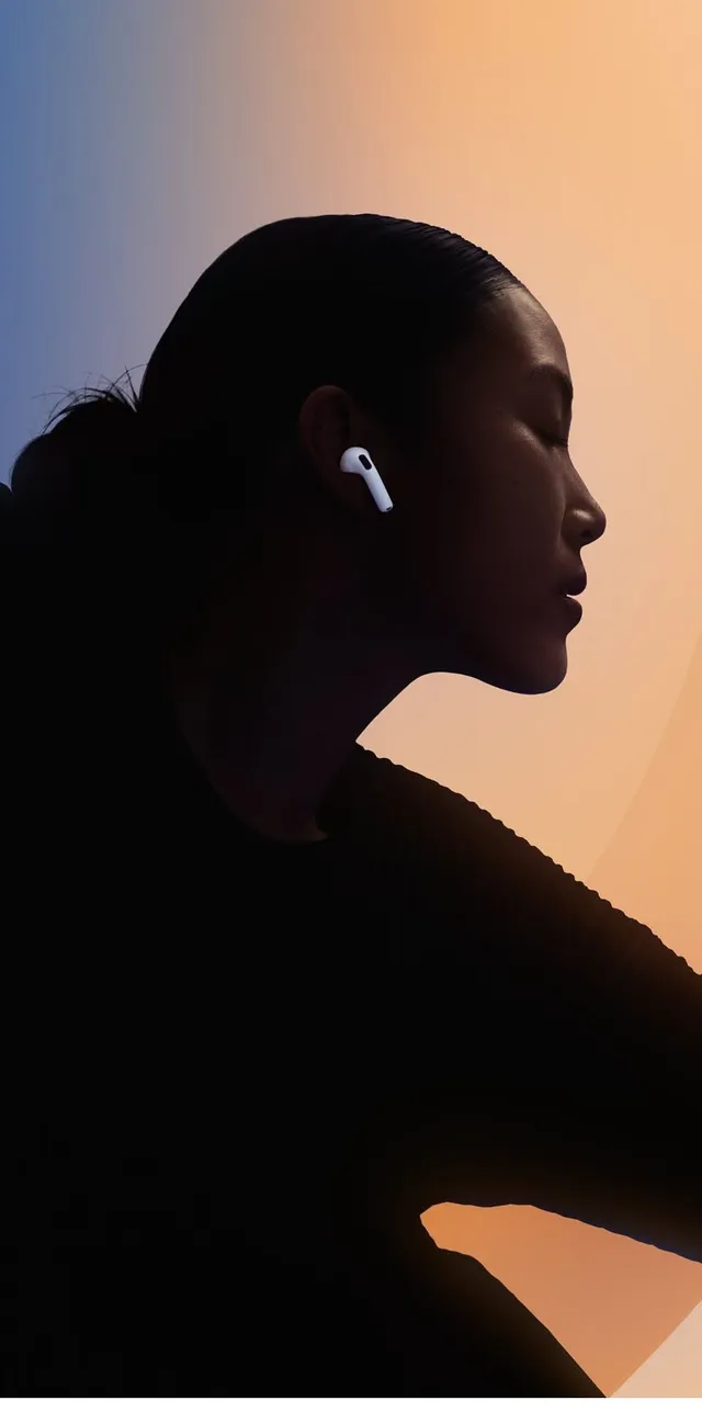 A striking silhouette of a woman wearing AirPods against a gradient background of warm orange and cool blue tones, evoking a modern, sleek vibe. The editorial photography emphasizes minimalism and sophistication, highlighting the technology seamlessly integrated into daily life.